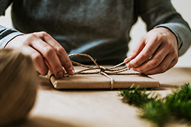 Close up photo of two hands wrapping a Christmas gift with brown paper and twine.