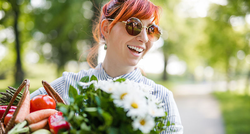 How to be sustainable - image of laughing girl wearing sunglasses carrying fresh fruit and flowers