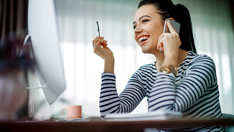 Young woman on the phone looking at computer and smiling