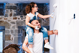 Dad with daughter on his shoulders painting a wall