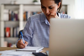 A woman looks focused while writing in a notepad in her office.