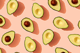 Several avocado halves sit upon a pink background.