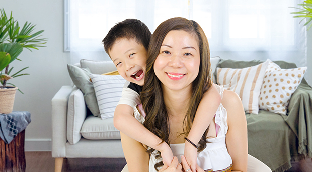 A young boy piggybacks his mum as both of them smile at the camera.