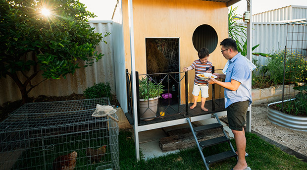 A father gives his son food next to a large cubby house.