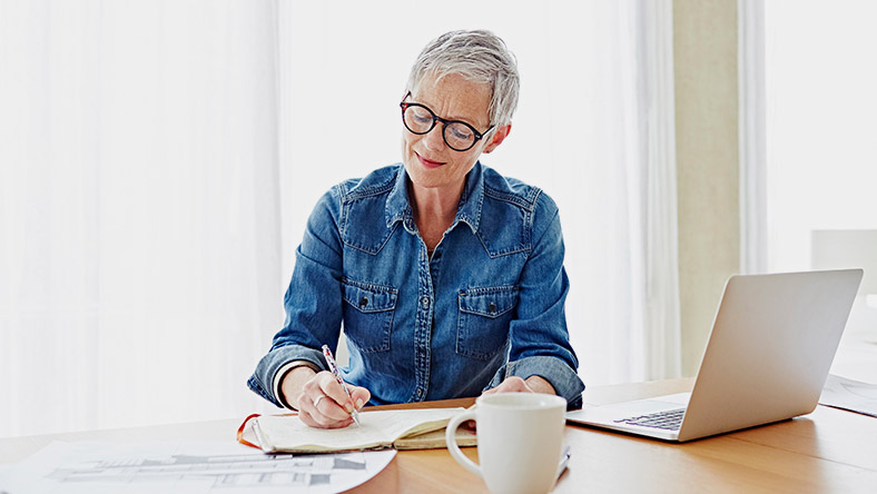 A woman sits at her desk with her lap top and financial papers, cleaning up her spending.