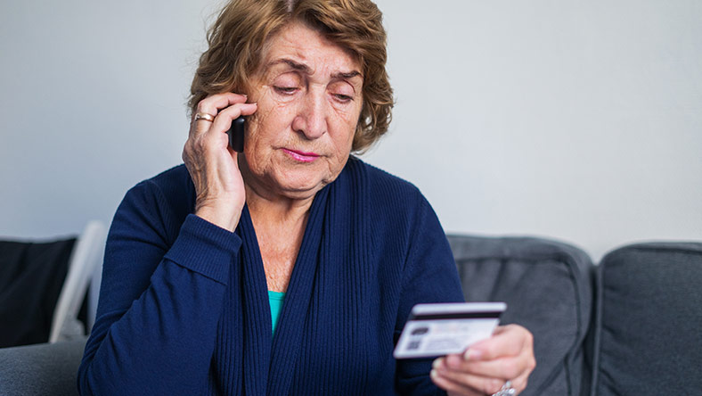 A woman reads her bank card while using the phone.