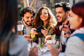 A group of people smiling and laughing while eating at an outdoor table.