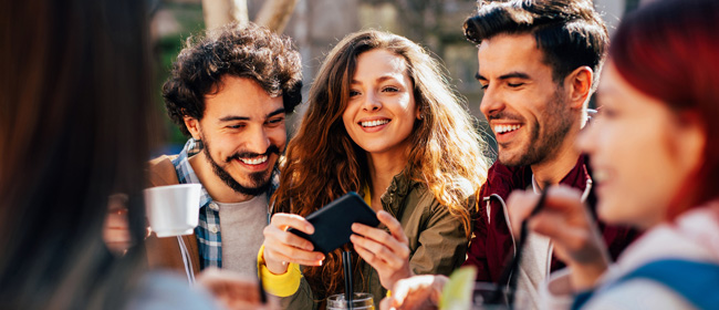 A group of people smiling and laughing while eating at an outdoor table.