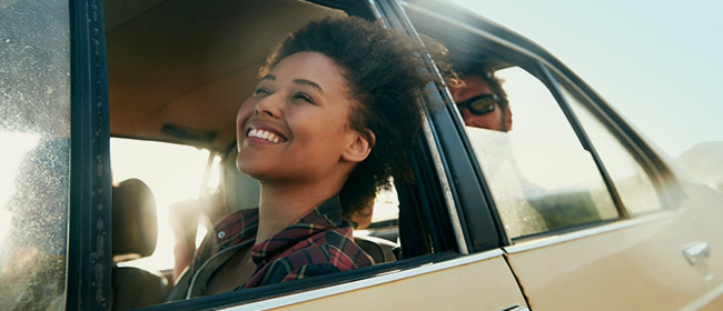 Young lady sitting in the front car seat with the window down and smiling 