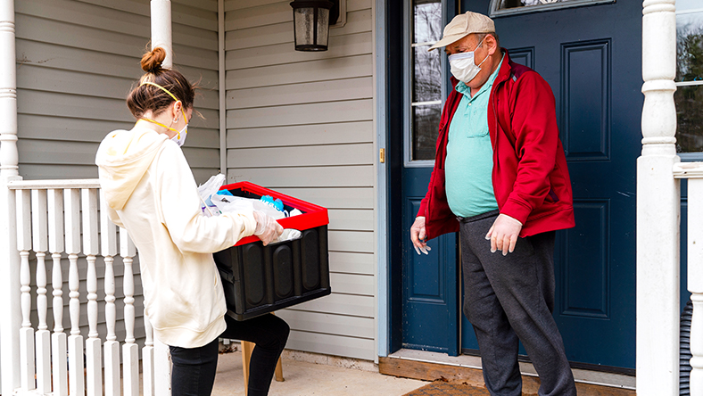 A woman wearing a mask dropping off a box for an older man, also wearing a mask.