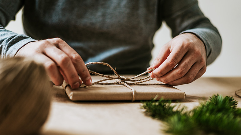 Close up photo of two hands wrapping a Christmas gift with brown paper and twine.