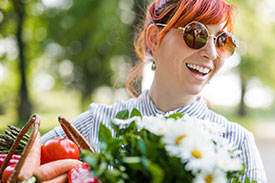 How to be sustainable - image of laughing girl wearing sunglasses carrying fresh fruit and flowers
