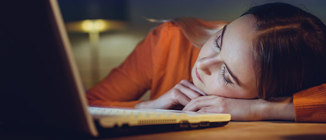 A female uni student sleeping in front of an open laptop.