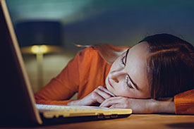 A female uni student sleeping in front of an open laptop.