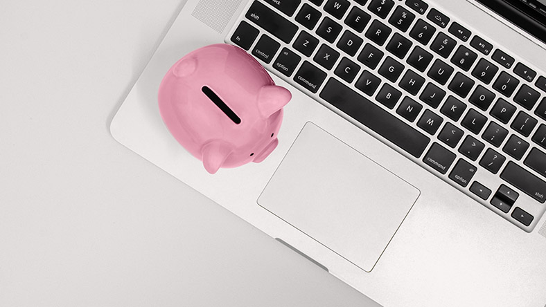 A piggy bank rests next to the keyboard of a laptop.