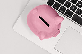 A piggy bank rests next to the keyboard of a laptop.