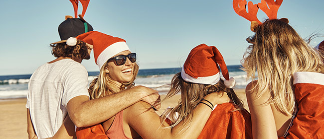 Four young adults smiling at the beach wearing Santa Claus hats and reindeer ears headband