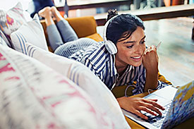 Lady with headphones on a couch using a laptop