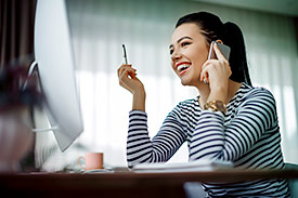 Young woman on the phone looking at computer and smiling