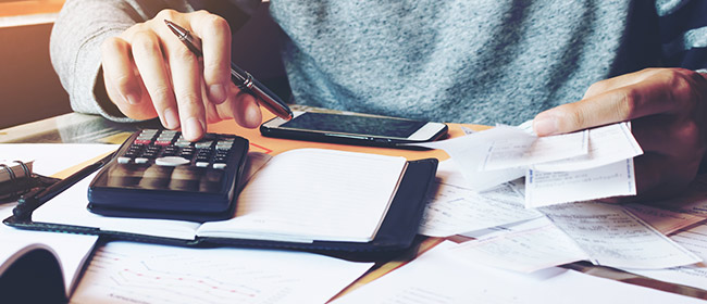 Person holding pen and tapping on calculator while going through receipts