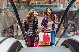 two women with shopping bags going up escalators 