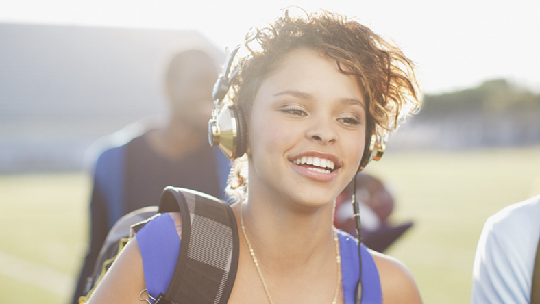 Female university student walking while wearing headphones and carrying backpack