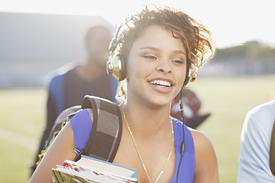 Female university student walking while wearing headphones and carrying backpack