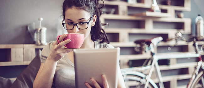 Young girl looking at her iPad while drinking a cup of coffee