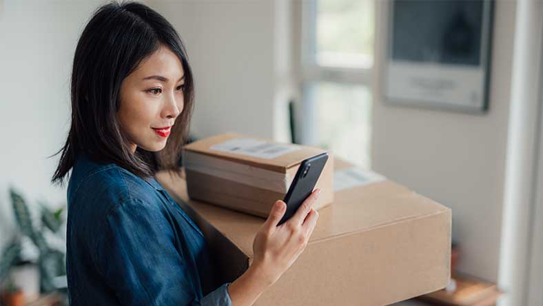Woman looking at phone while holding boxes
