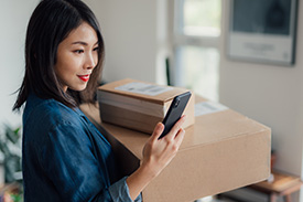 Woman looking at phone while holding boxes