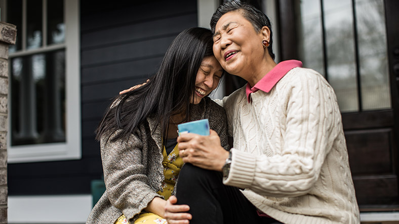 A mother and her daughter embrace sitting on their front steps.