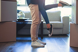 A man lifts his partner's feet in the air as they celebrate in their first home.