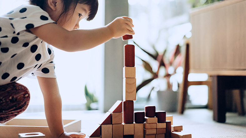 A young girl constructs a tower from wooden building blocks