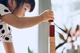 A young girl constructs a tower from wooden building blocks