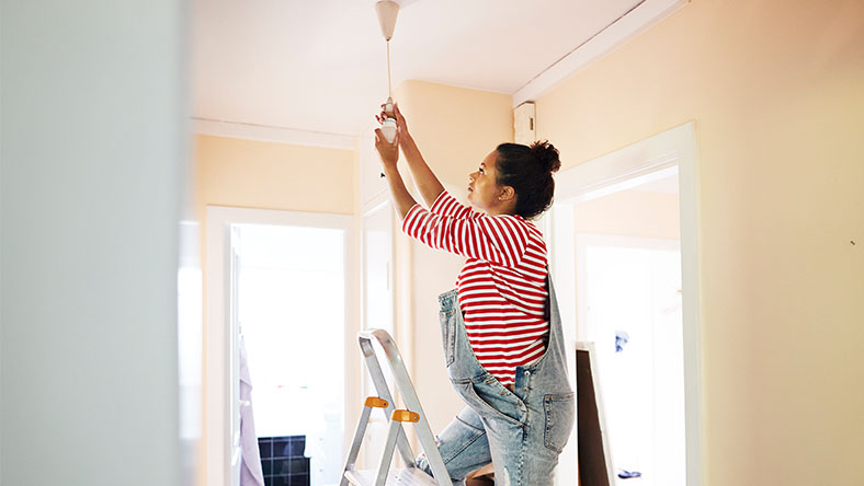 A young woman on a step ladder changes her light fixtures.