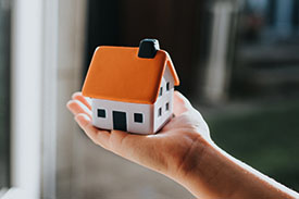 A tiny toy house sits in the palm of someone's hand.