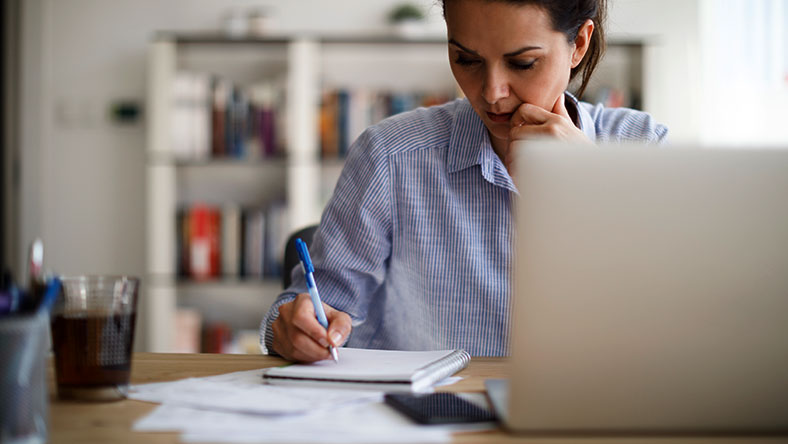 A woman looks focused while writing in a notepad in her office.