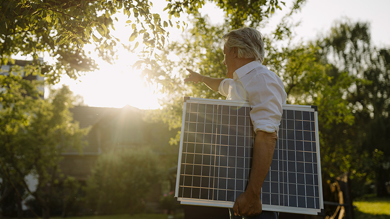 A man holds a solar panel under his arm on a sunny day.