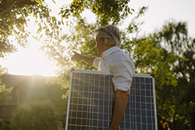 A man holds a solar panel under his arm on a sunny day.