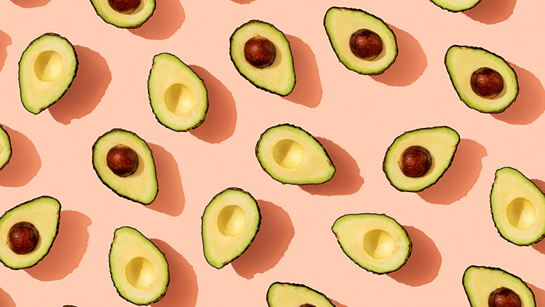 Avocado halves on pale pink background