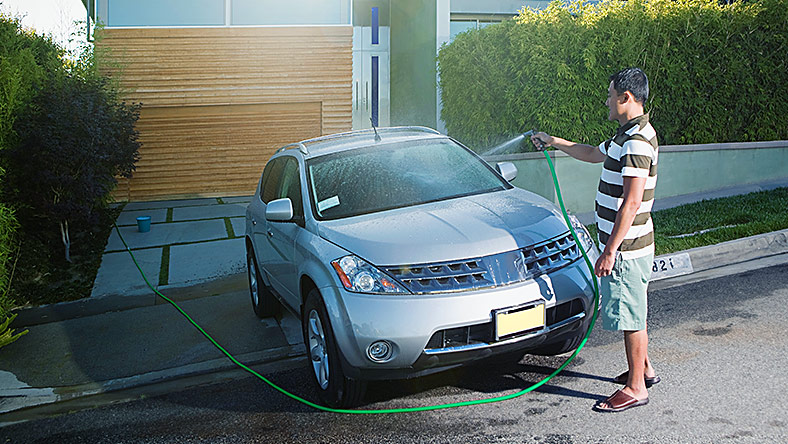 Man cleaning car with hose in his driveway