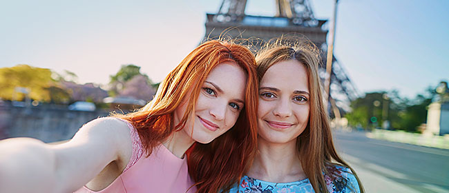 Two young women posing for a selfie in front of the Eiffel Tower