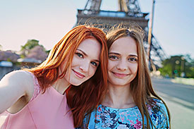 Two young women posing for a selfie in front of the Eiffel Tower