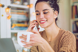 Young woman smiling with her phone up to her ear and holding a white mug in her other hand