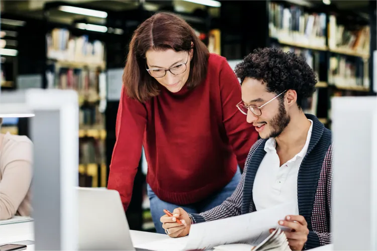 Two students are working together at a computer station in a library.