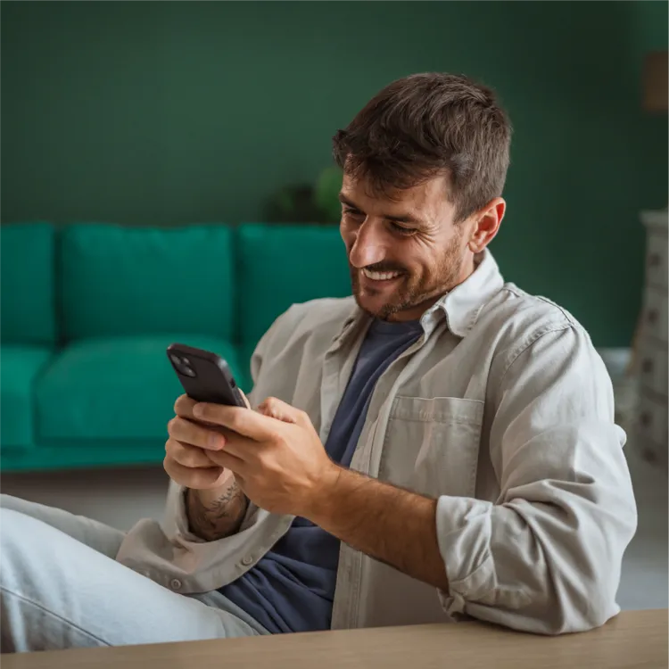 A young man reclines on a sofa while using a smartphone.
