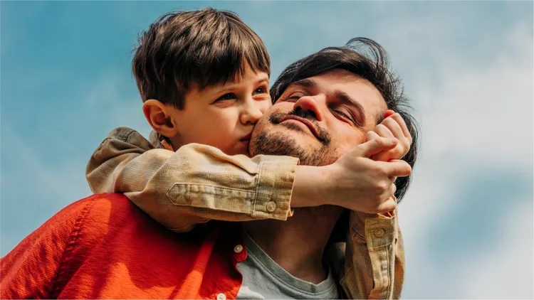 A child is held up high above an adult's shoulders on a beach.