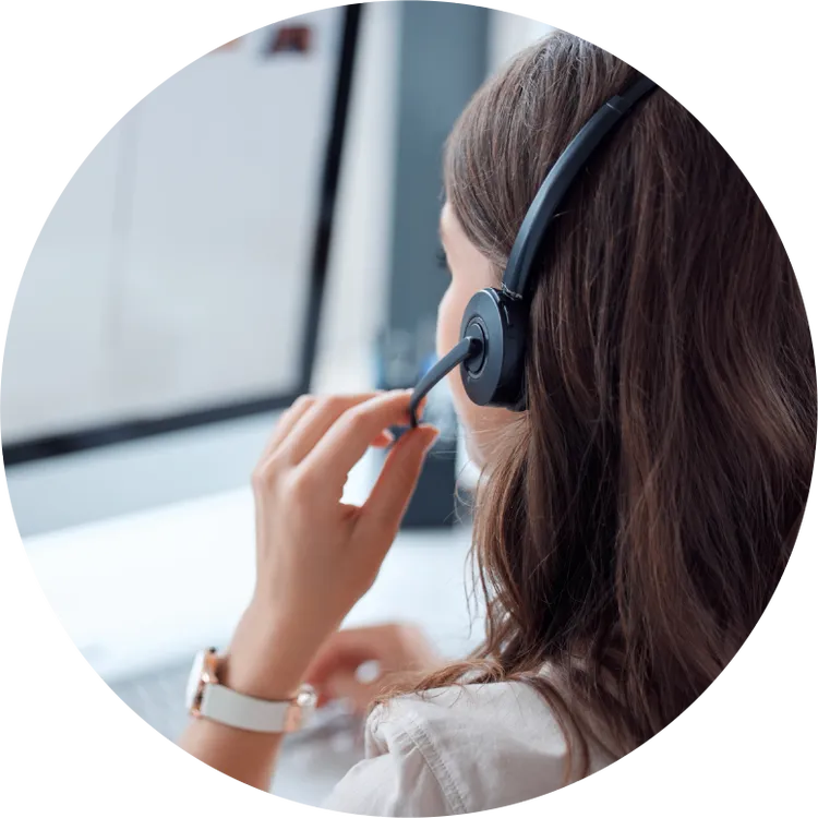 A young woman is seen from behind, wearing a headset and working at a computer.