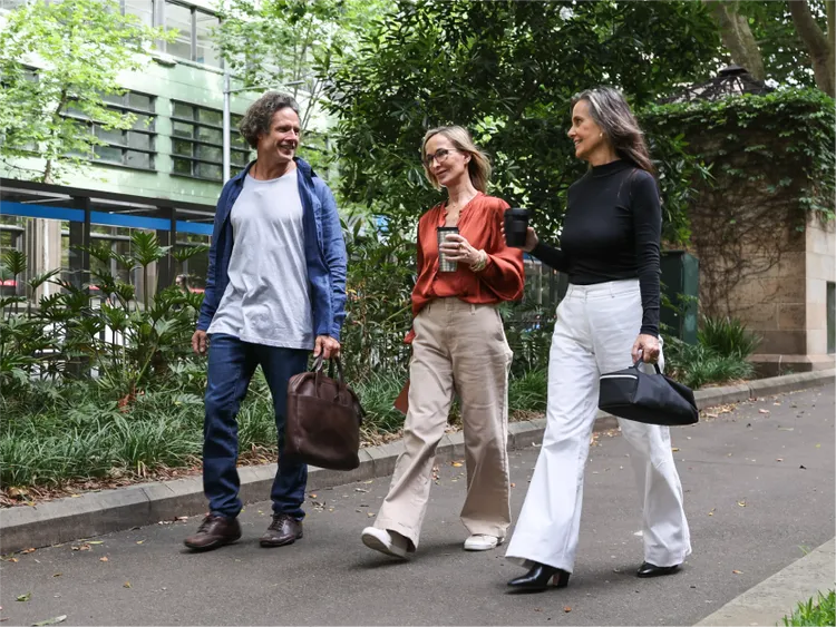 Three adults walk together along a paved path in an urban park setting.