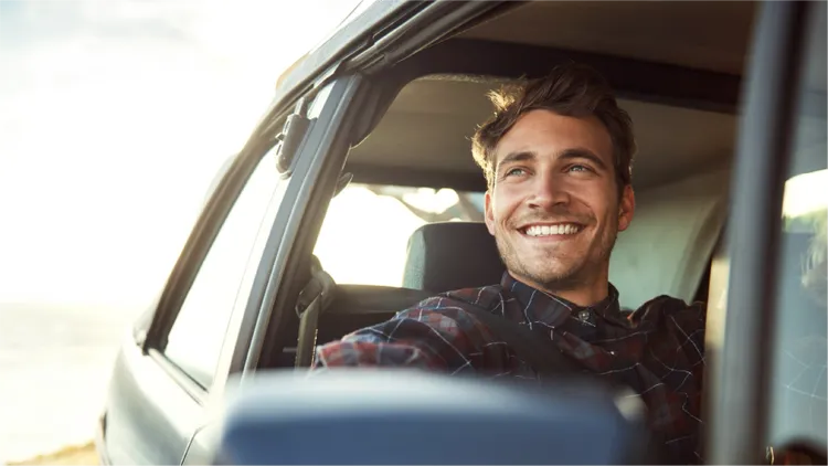 A man sits in the front seat of a car with the window open, leaning back comfortably.